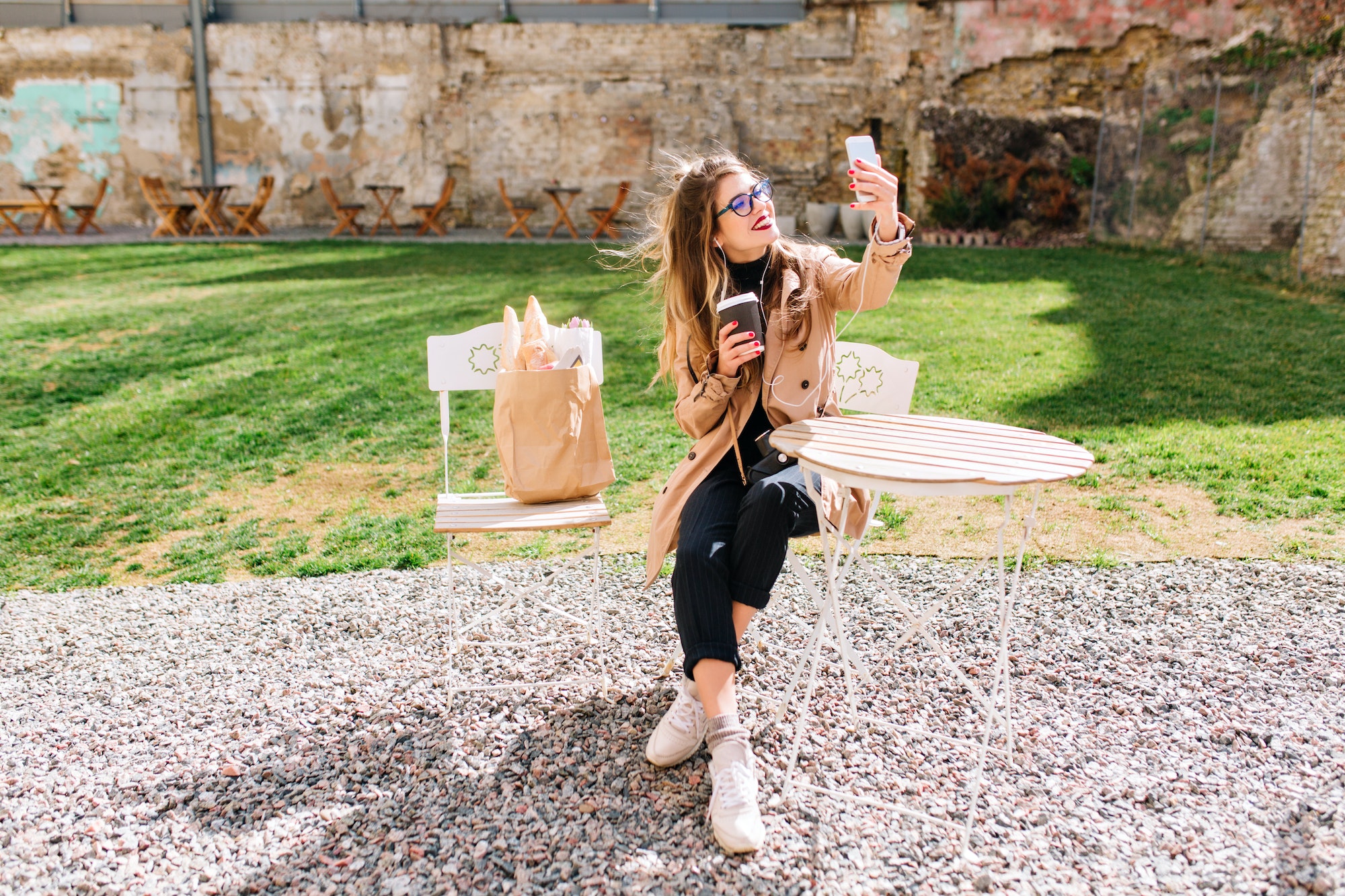 Attractive hipster girl wearing beige coat makes selfie for instagram profile during coffee break in