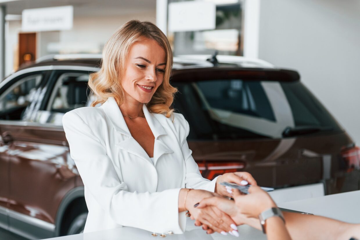 Paying for the product. Woman in formal clothes is indoors in the autosalon