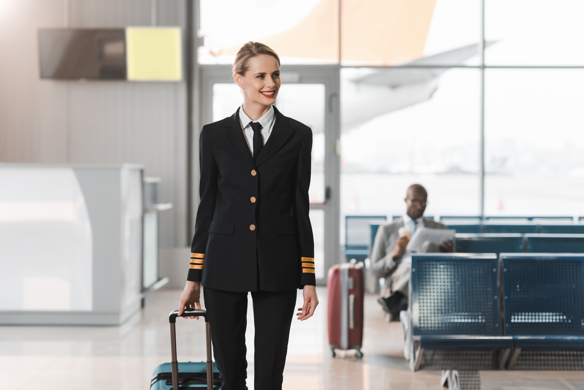 smiling female pilot with suitcase walking by airport lobby