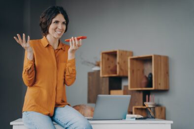 Happy hispanic female employee using speakerphone or virtual voice assistant on mobile phone